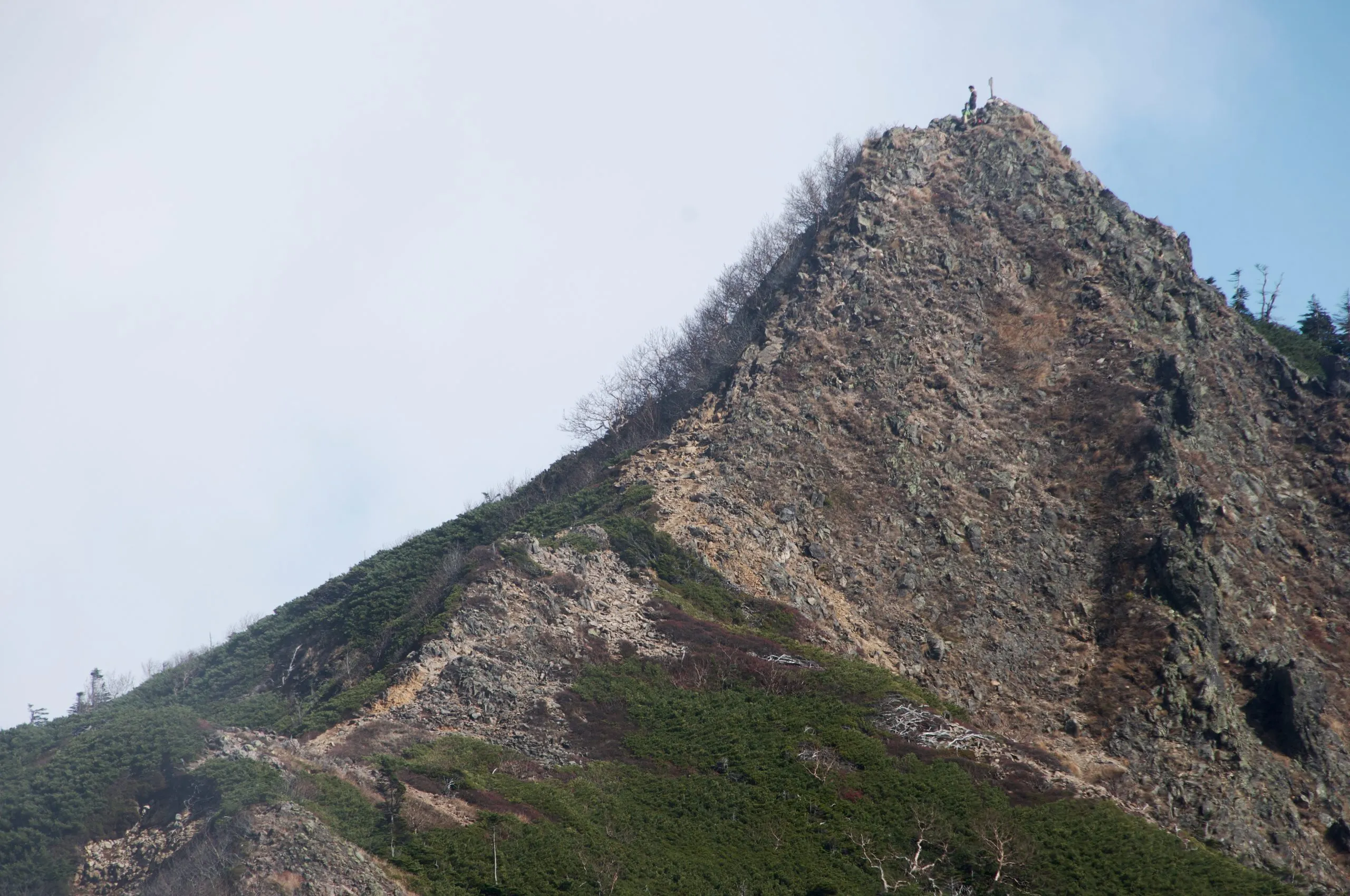 Rocky summit pyramid with a hiker at the marker, Nyoho Mountain hiking trail, Nikko Japan
