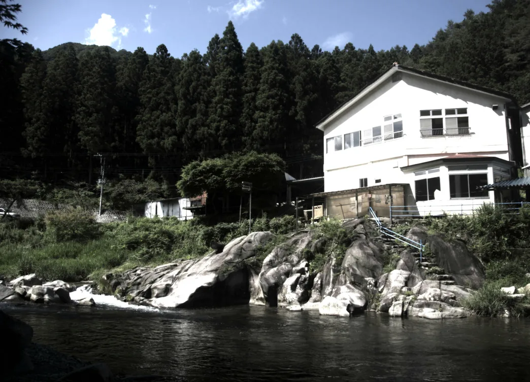 Earth Hostel seen from across the Kurokawa River, with rocks and steps down to the water