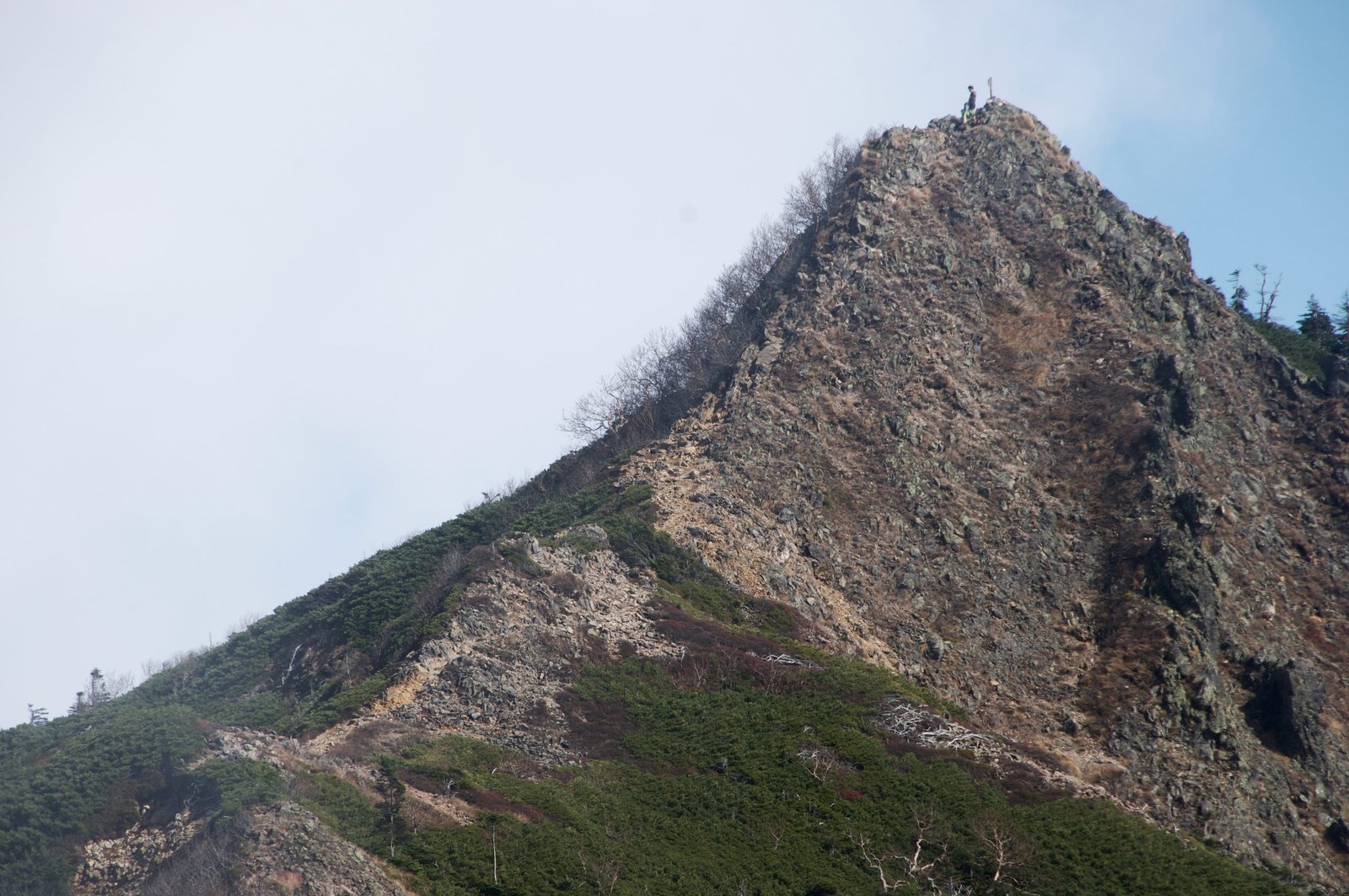 Rocky summit pyramid with a hiker at the marker, Nyoho Mountain hiking trail, Nikko Japan